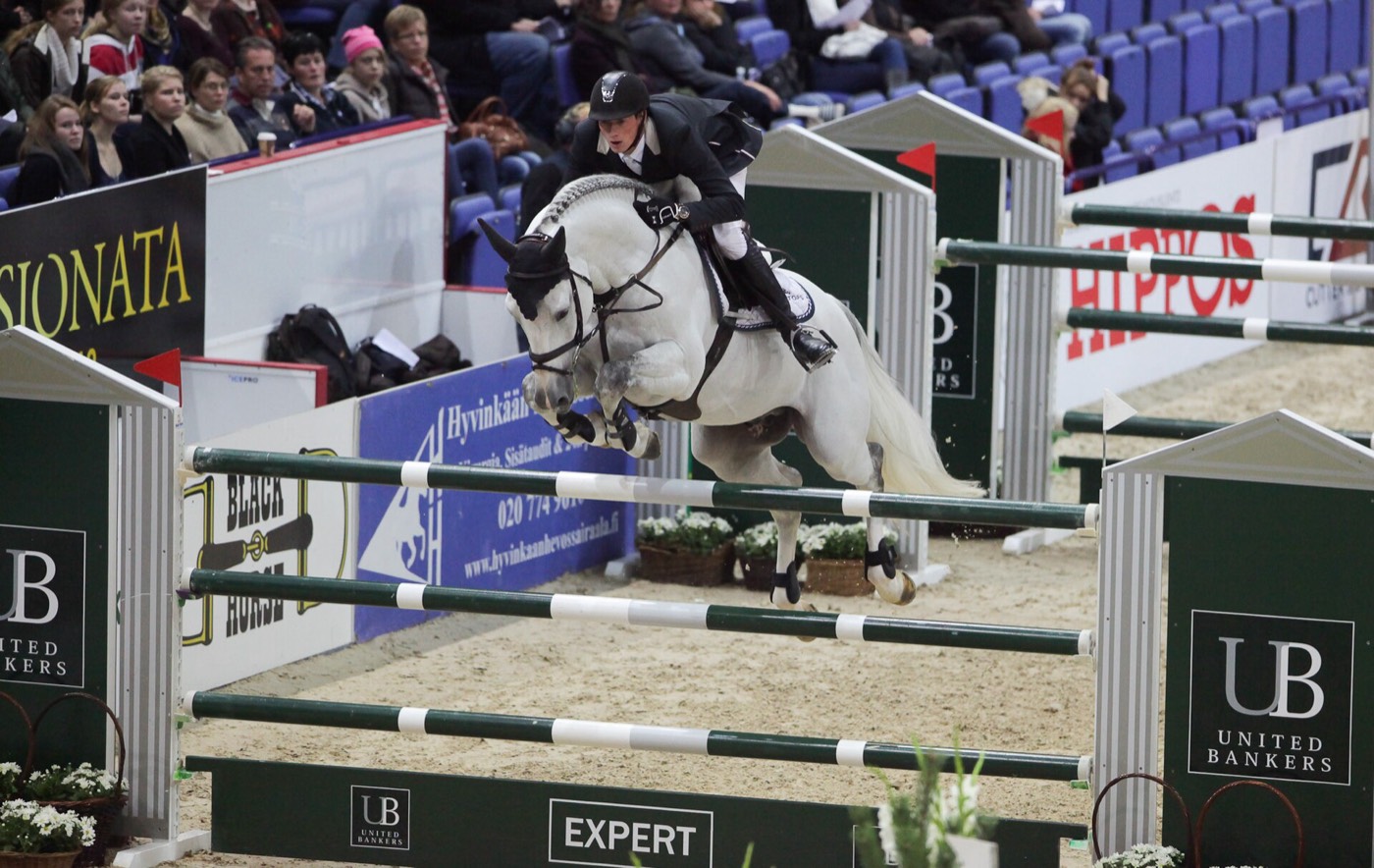 A rider and grey horse jumping a fence at a horse show